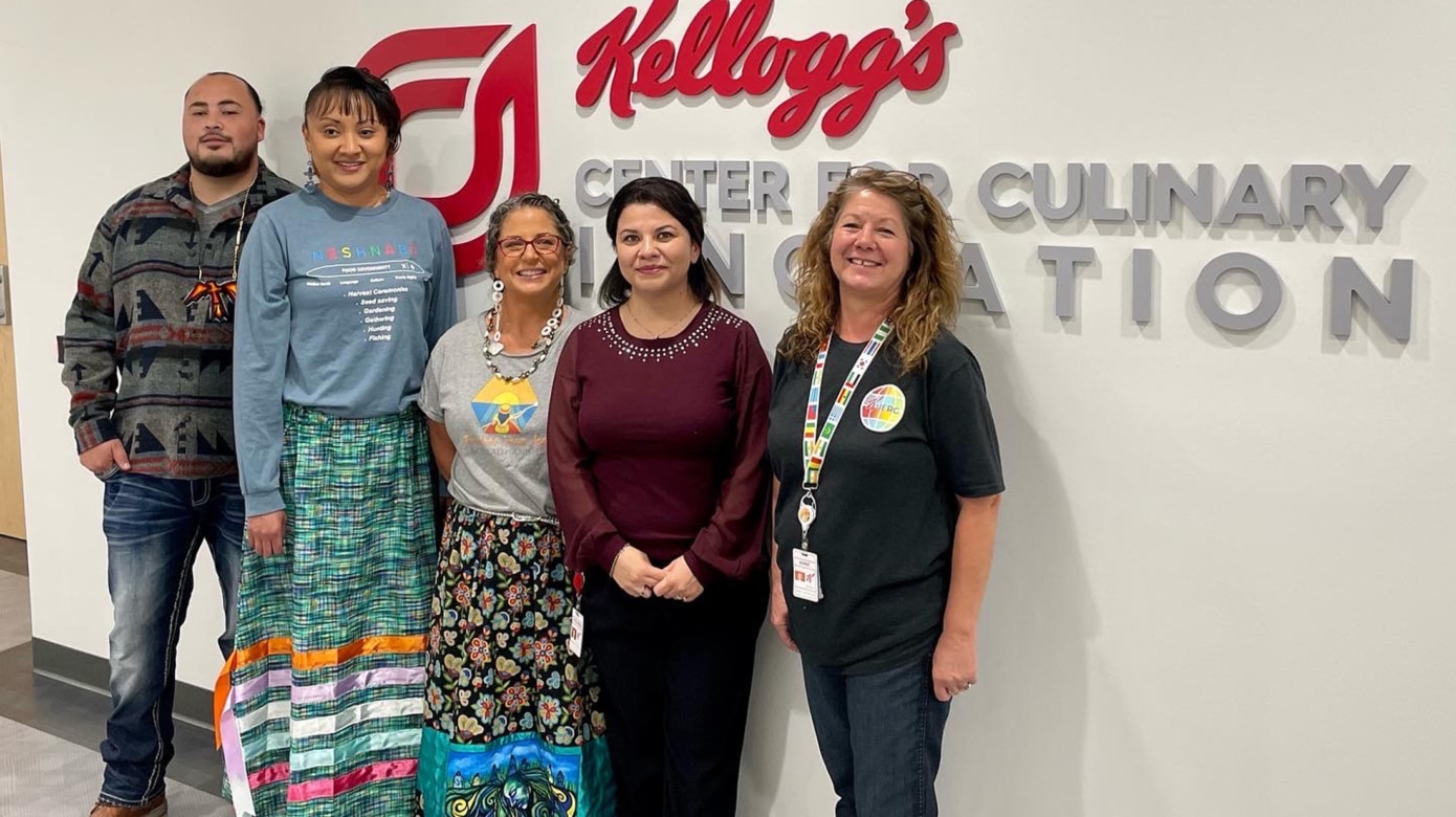 Nottawaseppi Huron Band Potawatomi Kevin Harris and Nickole Keith, Citizen Potawatomi Nation Jody Ghzadawsot matennna, and Kellogg's Giovanna Hernandes Pemeneggie and Anne Dickinson pose for a photo in front of a sign for Kellog's Center for Culinary Innovation.