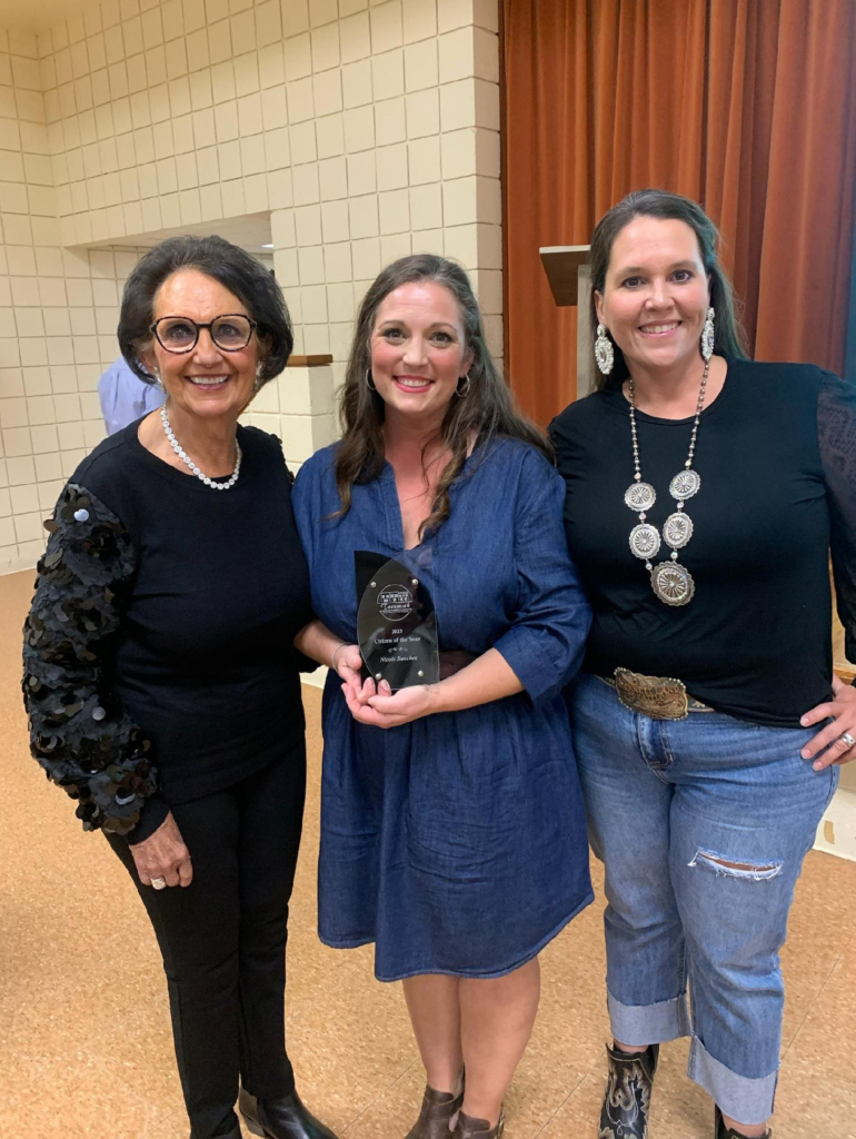 Nicole Sanchez, center, wearing a blue dress and holding an award plaque is framed by CPN Vice-Chairman Linda Capps, wearing all black and a string of pearls, and Stacey Bennett, wearing a black shirt and blue jeans.