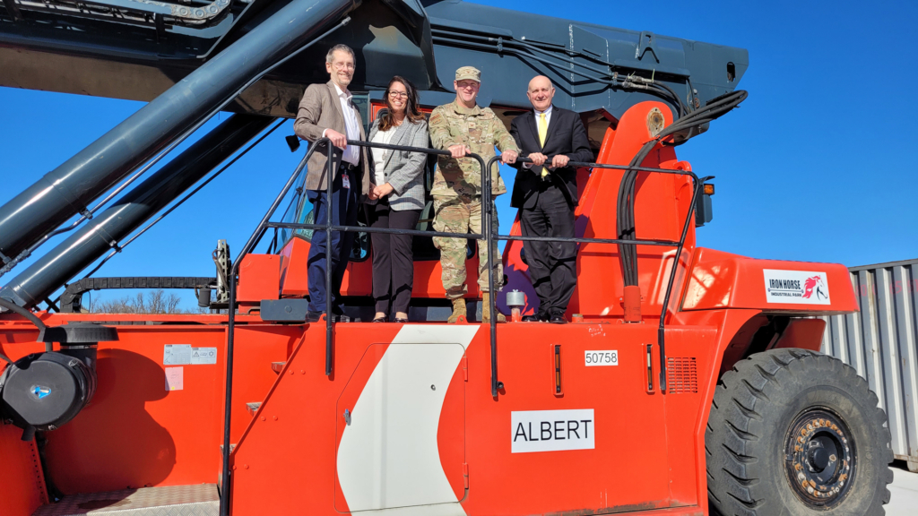 Air Force Sustainment Cnter personnel and CPN's Dr. Jim Collard pose for a photograph atop Iron Horse Industrial Park's orange transload machinery.