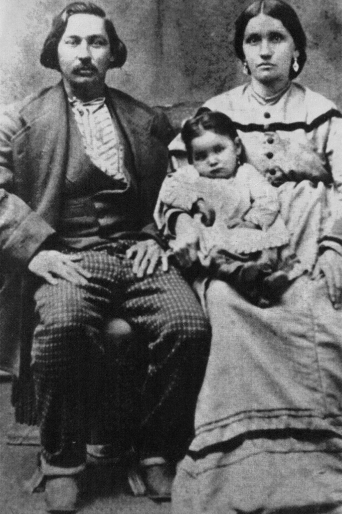 Archival photo of young Alexander and Zoa Rhodd, dressed in a suit and long dress respectively, seated and holding a child.