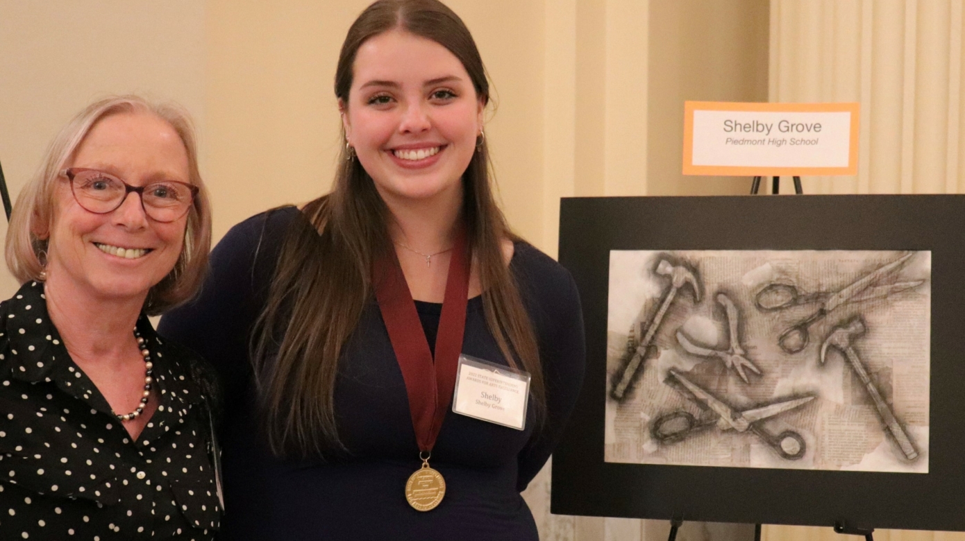 CPN tribal member Shelby Grove, with long hair parted in the middle and an awards medal around her neck, poses with her art teacher, Frances Williams, and her artwork "Tools," a charcoal drawing for which she won a State Superintendent Award for Arts Excellence.