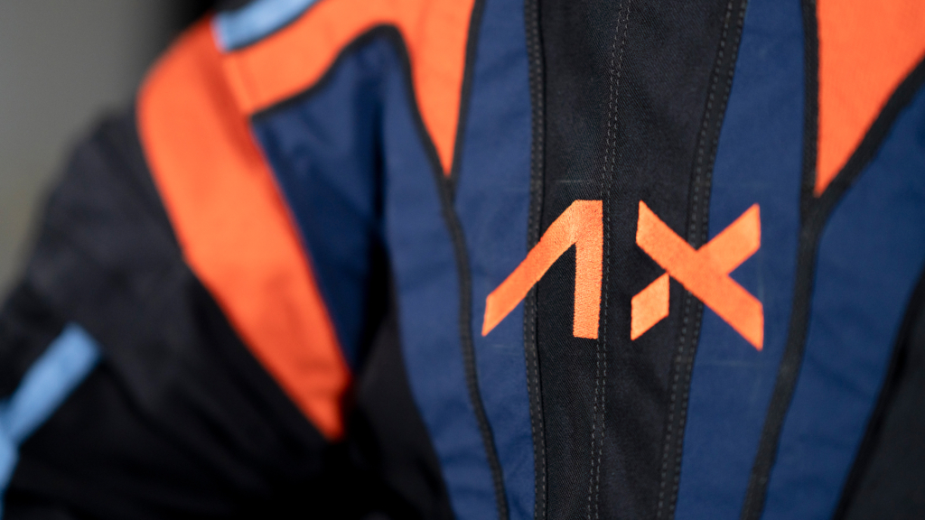 A close-up of the orange logo for the Axiom Space AxEVA spacesuit on the navy blue and black fabric of the suit.