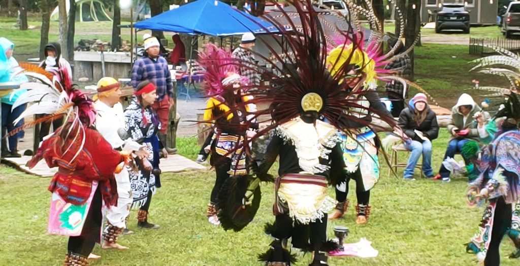 Action shot of a group of dancers in an outdoor dance arena with spectators seated around the perimeter.