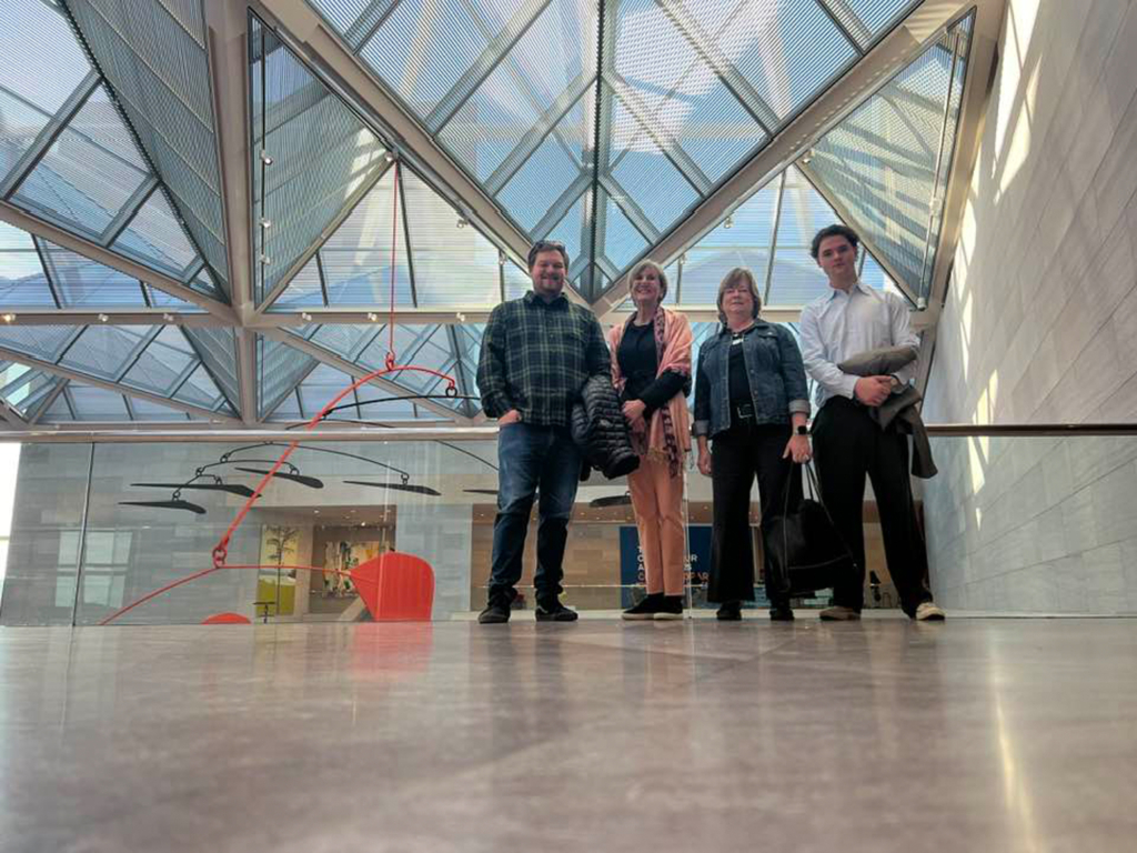Group shot from a low angle of four CPN members in an atrium with a geometric glass roof.