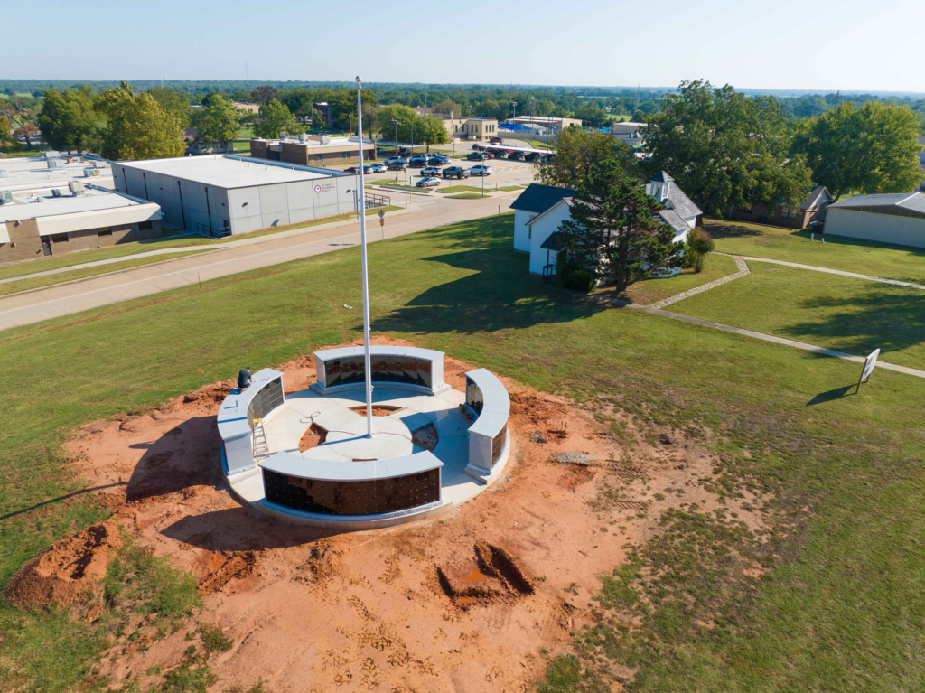 Areial shot of a round structure in a red clay area surrounded by gass.