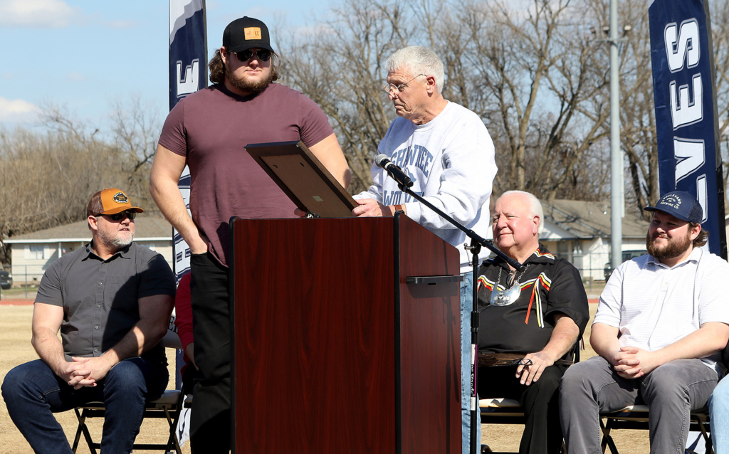 Shawnee Mayor Ed Bolt, wearing a Shawnee Wolves sweatshirt, hands a framed award to Creed Humphrey at Jim Thorpe Stadium. 