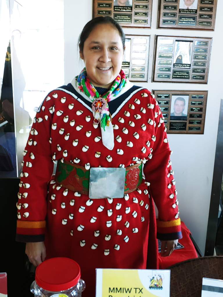 A person wearing a red dress with white elk's teeth and bound by a wide green and red belt with large square buckle.