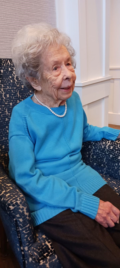 Dr. Rosemary Schrepfer, 101, seated in a printed arm chair and wearing a blue sweater and pearl necklace.