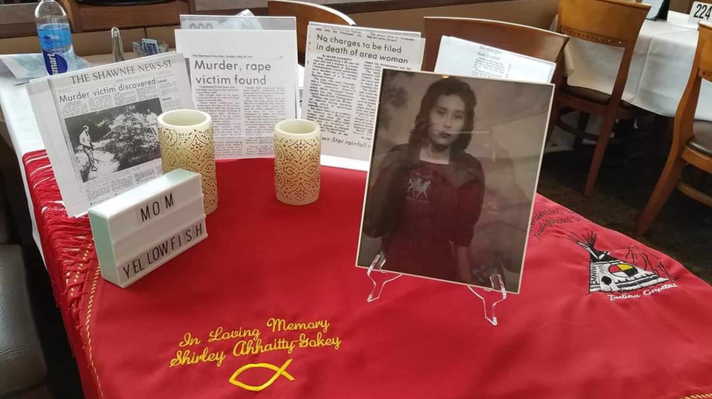 Memorial photos, news articles and candles on a red shawl embroidered in honor of Shirely Ahhaitty Gokey.