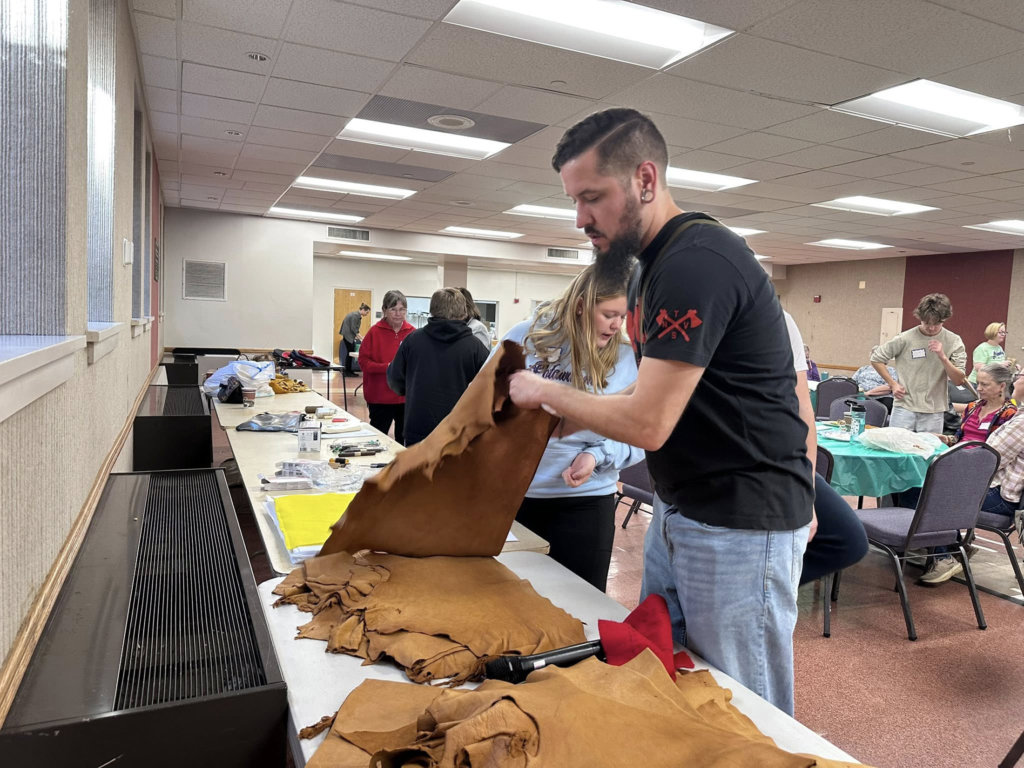 Image of a Tribal member wearing a T-shirt and jeans works with a piece of leather for moccasin making.