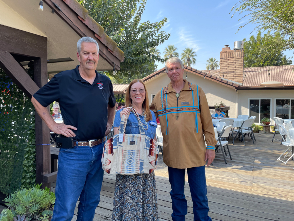 Two CPN Legislators stand with a Tribal member holding a Pendleton duffel bag.