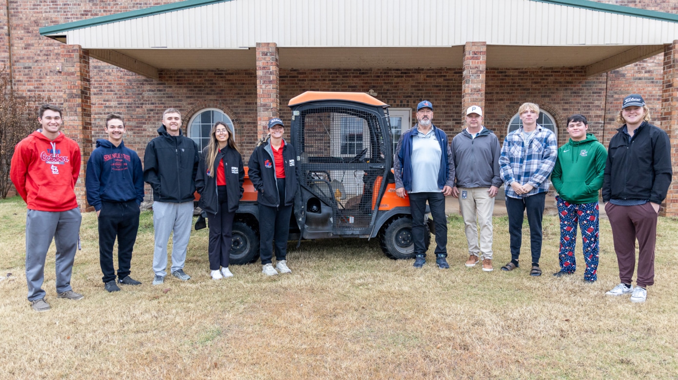 A group stands next to an orange and black utility golf cart.