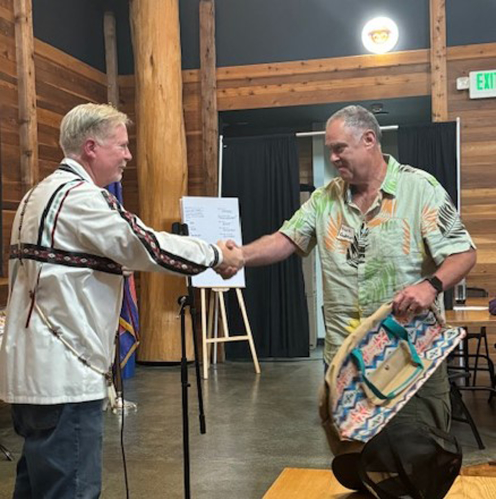 Dave Carney shakes hands with a Tribal member in a Hawaiian print shirt.