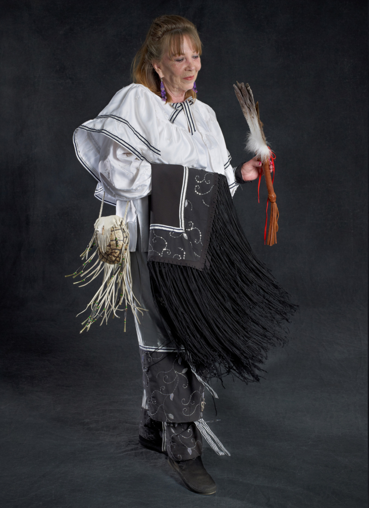 Portrait of Gene Lambert in white and black regalia, holding a black shawl and feather fan. Portrait by Sharon Hoogstraten.