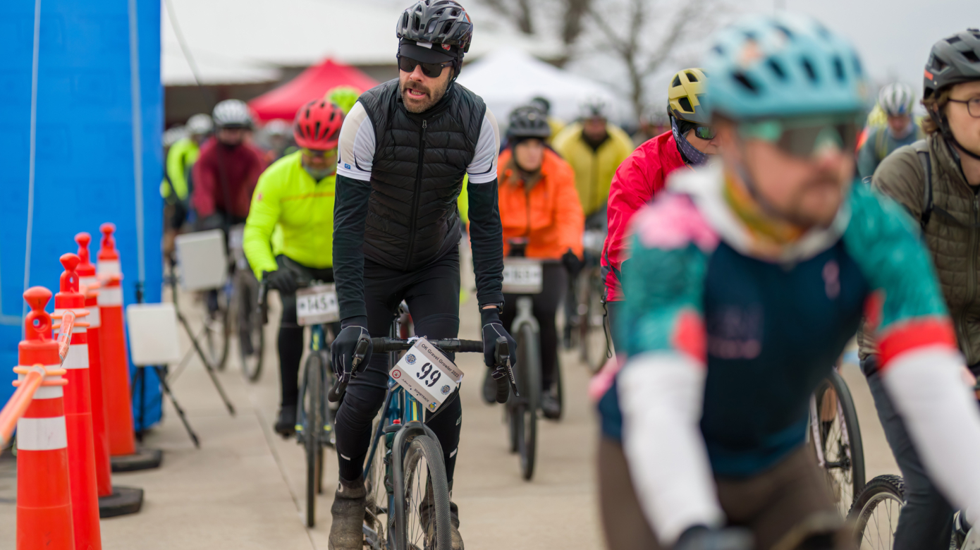 Among a group of cyclists in colorful gear, CPN employee George Wright stands on his bike pedals and looks over his shoulder as he begins the 2023 Gravel Growler race.