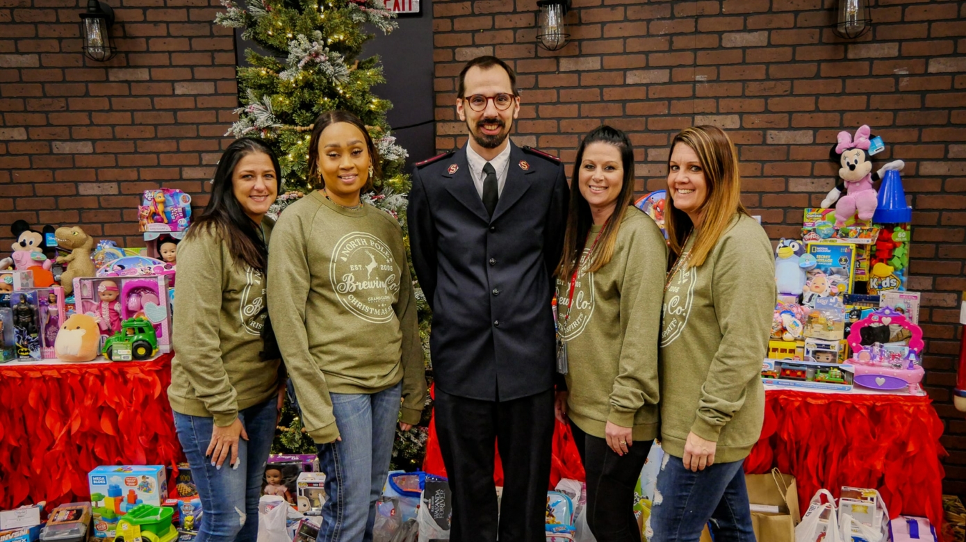 Four employees in green sweatshirts stand next to a Salvation Army captain in uniform.