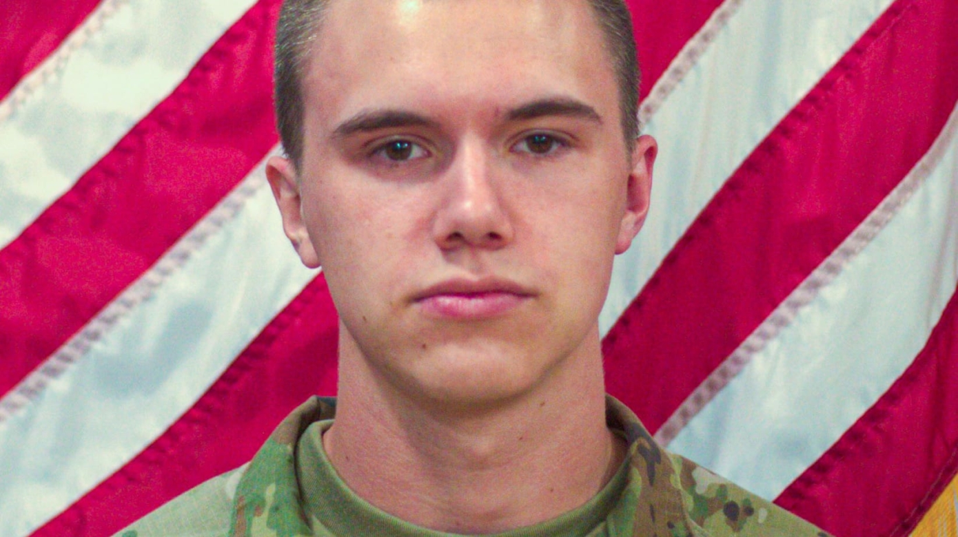 Headshot of a man in U.S. Army fatigues in front of an American flag.