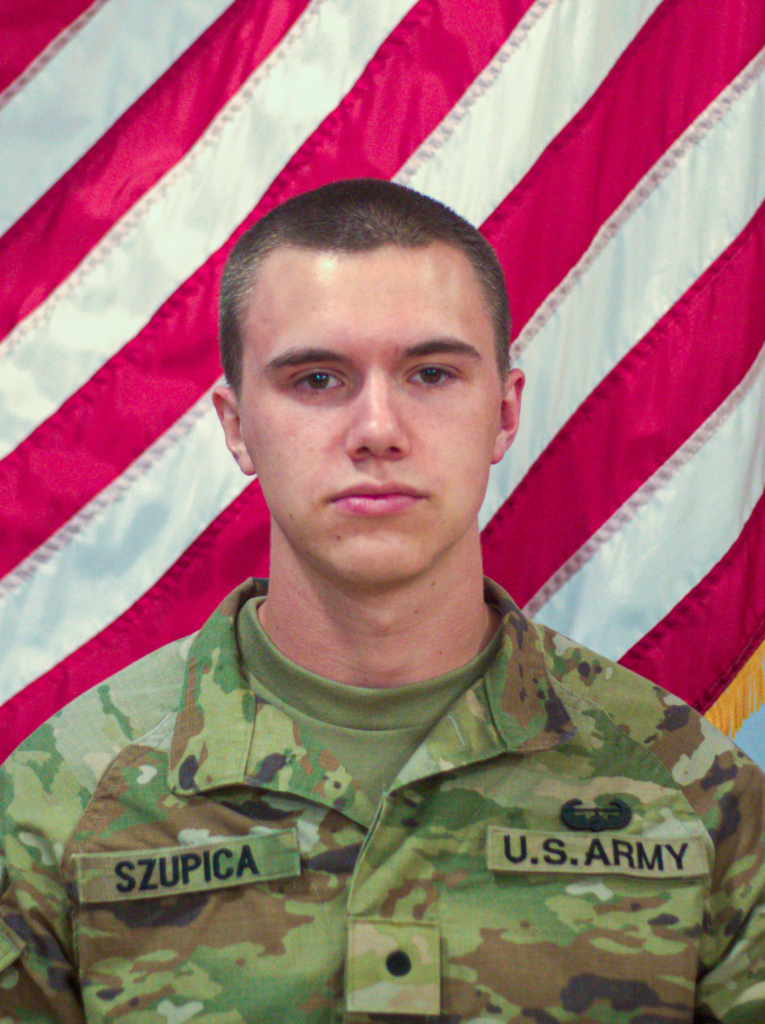 Headshot of a man in U.S. Army fatigues in front of an American flag.