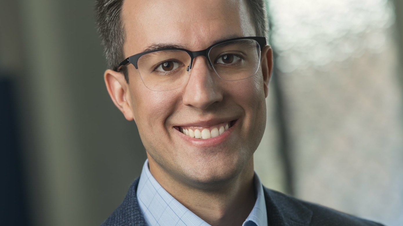 Headshot of CPN tribal member Andrew Mock. Wears glasses with dark upper rims, and a navy suit and light blue check shirt.