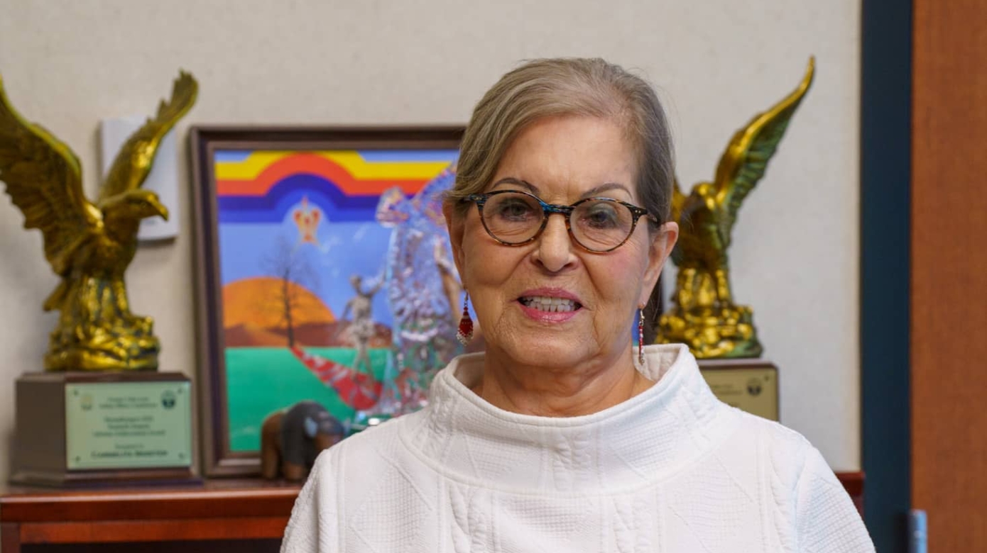 A person in a white turtleneck sweater, black glasses, and gray hair pulled back behind their head holds an award shaped like a flame.