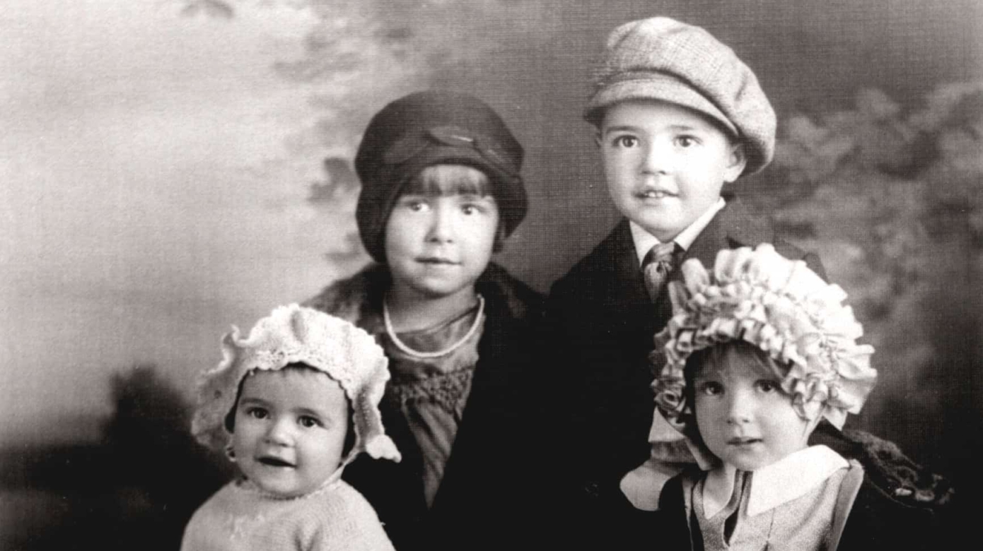 Black and white photograph of four children, the two oldest standing and the two youngest seated in front of them.