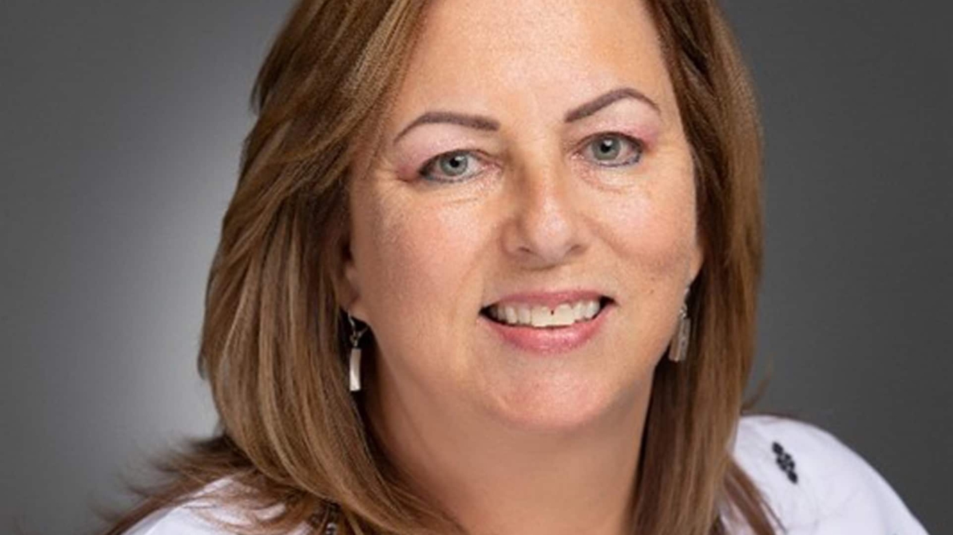 Headshot of Karla Bylund wearing a white blouse with black geometric designs. She has shoulder-length brown hair and light eyes.