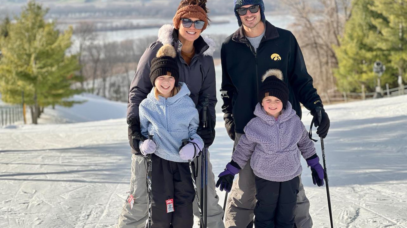Two adults and two children in ski pants, jackets and hats stand on a snow covered slope for a family photo.