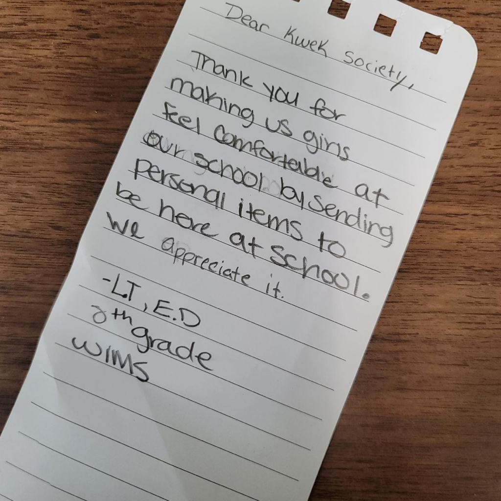 A photograph of a handwritten note reading: Dear Kwek Society, Thank you for making us girls feel comfortable at our school by sending personal items to be here at school. We appreciate it. - LT, ED. 8th Grade. WIMS.