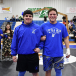 Lane Gourley and his best friend Chadd Kriz stand interlocked at the elbows and smiling at the camera at a wrestling event. The two are sporting blue and black, their high school's colors.