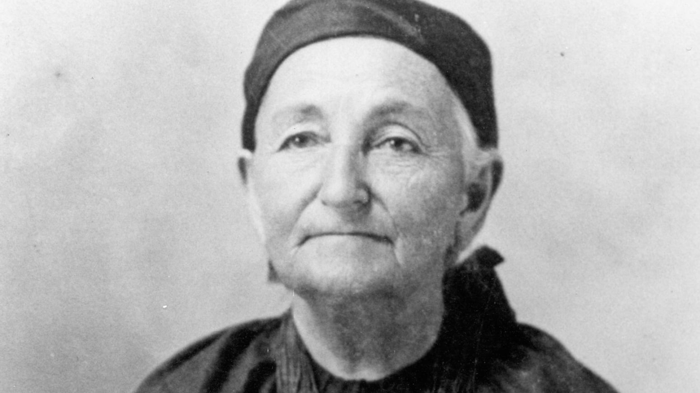 A black and white portrait of Mary Anderson Bourbonnais. She wears a ribbon shirt and layers of beaded necklaces.
