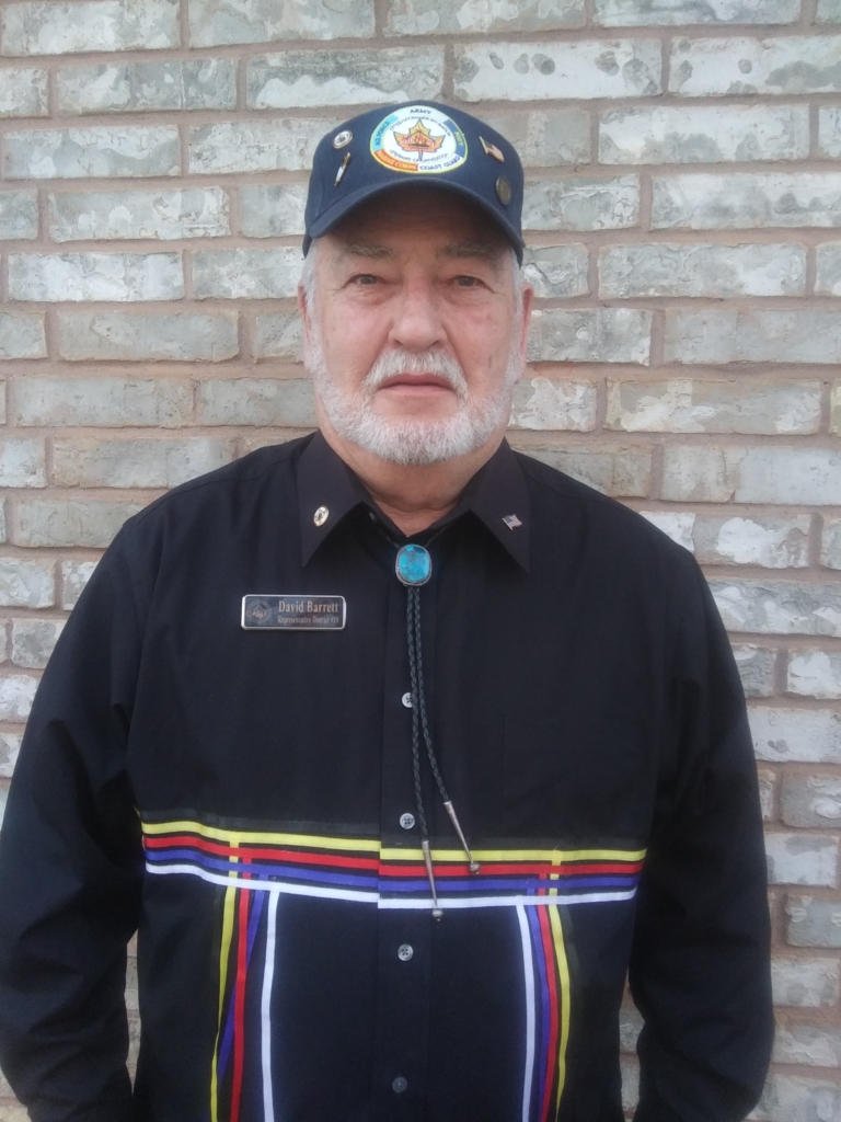 Headshot of CPN District 10 legislator David Barrett. Barrett wears a black ribbon shirt with yellow, red, blue, and white ribbons, as well as a turquoise bolo tie and an armed services ball cap.