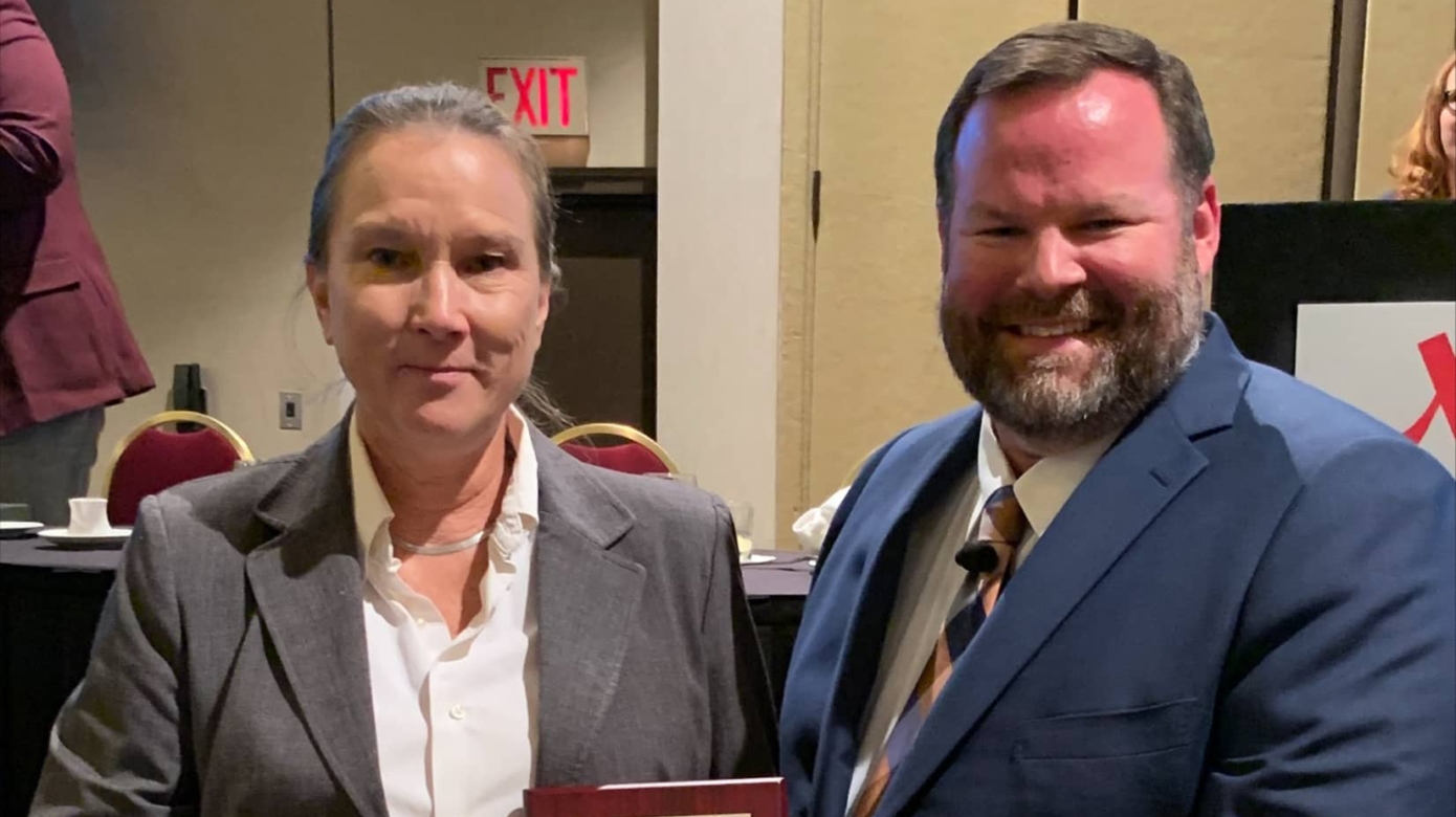 CPNPD Dispatcher Joan Nevin, left, wears jeans, a white blouse, and grey blazer. She accepts a plaque honoring her as Oklahoma Telecommunicator of the Year for 2022.