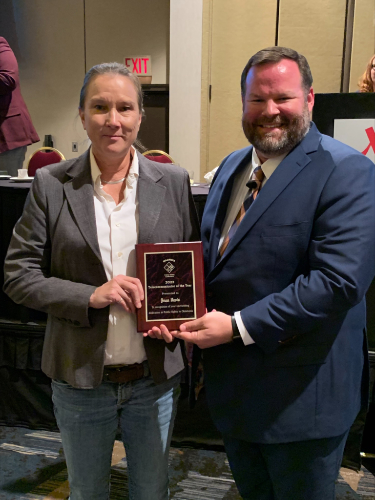 CPNPD Dispatcher Joan Nevin, left, wears jeans, a white blouse, and grey blazer. She accepts a plaque honoring her as Oklahoma Telecommunicator of the Year for 2022.
