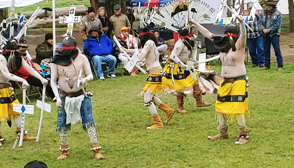 Action shot of a group of dancers in an outdoor dance arena with spectators seated around the perimeter.