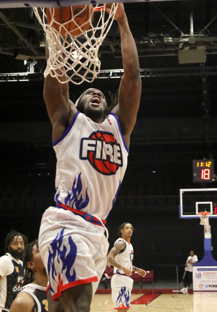 A Potawatomi Fire player is photographed mid-dunk, looking up open-mouthed at the ball as it passes through the net and still touching the rim with both hands.