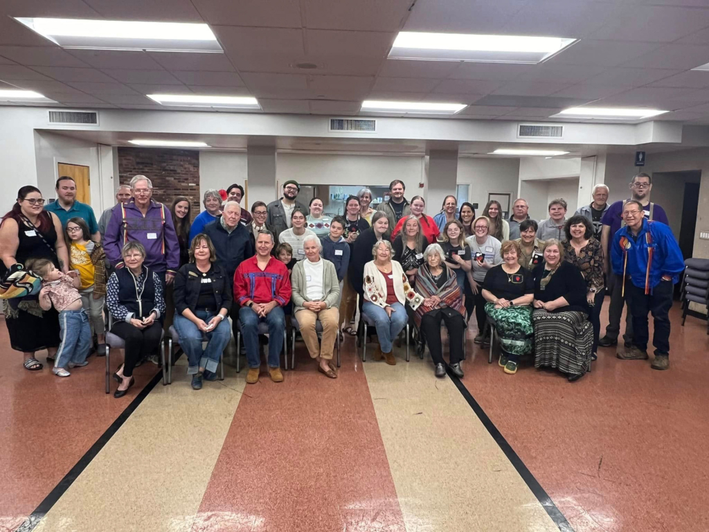 A large group of people gather for a photograph in a large meeting room.