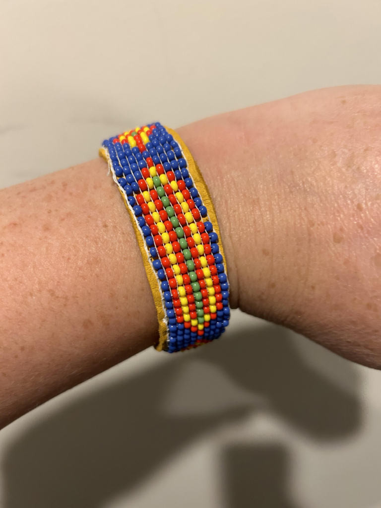 A freckled wrist with a blue, red, yellow, and green beaded band around it.