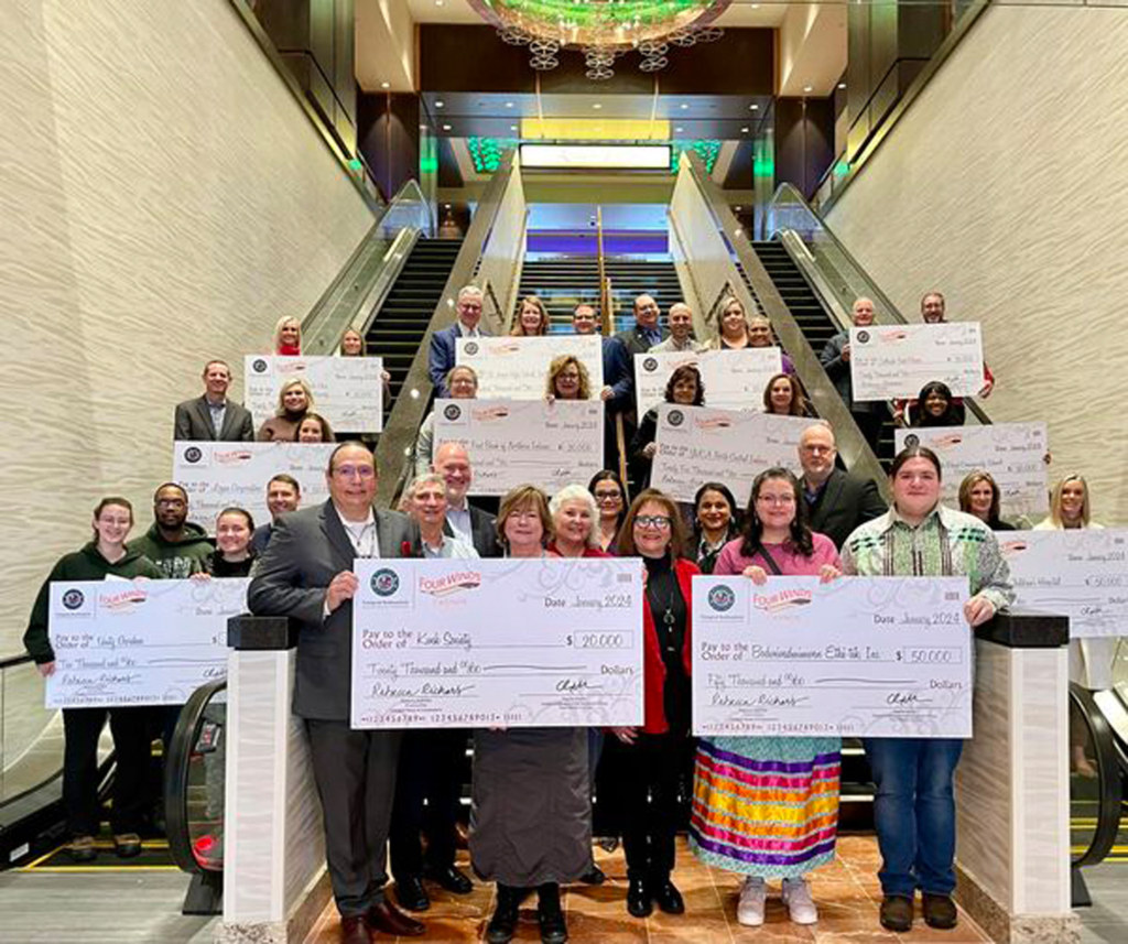 A group of about 30 people stands in a stairwell holding oversized symbolic checks.