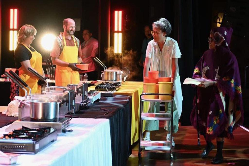 Eva Marie Carney and Alan Melot stand behind a display table wearing yellow aprons.