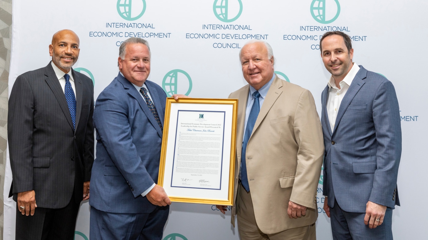 Tribal Chairman John "Rocky" Barrett poses with members of the international Economic Development Council in front of a IEDC logo wall. He holds his award, framed in gold, for leadership and public service.