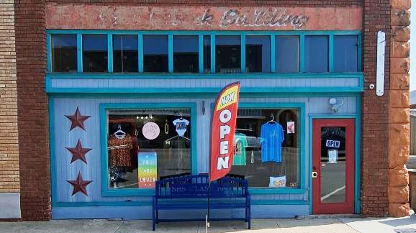 The storefront of the Treasure Box in Stroud, Oklahoma. The storefront is painted bright blue, which contrasts with the red brick of the building. A red "open" flag flies in front of the building.