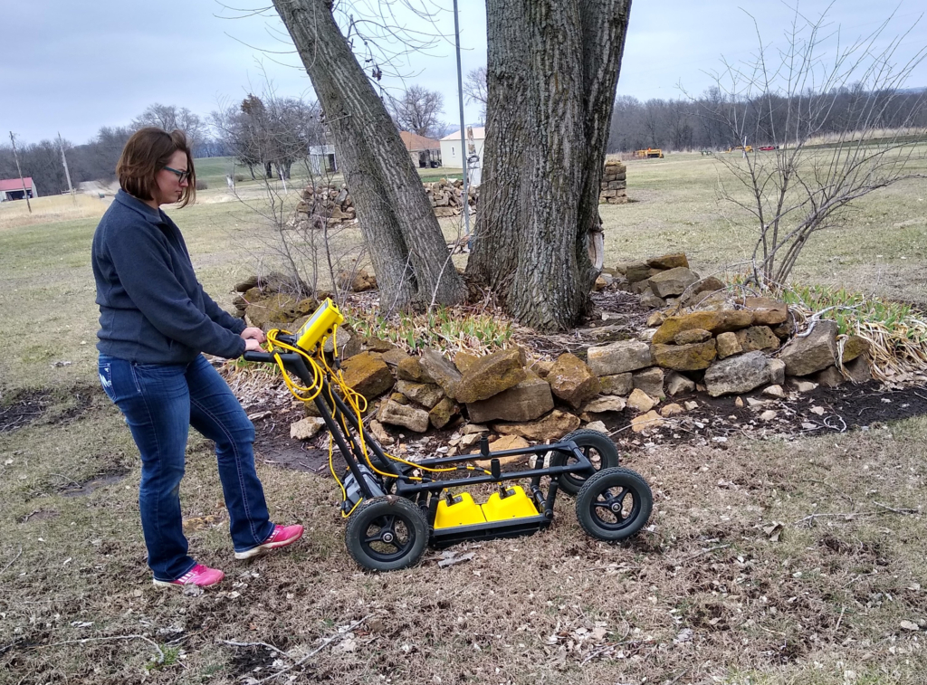 A person pushes a machine with bright yellow sensors across the ground.
