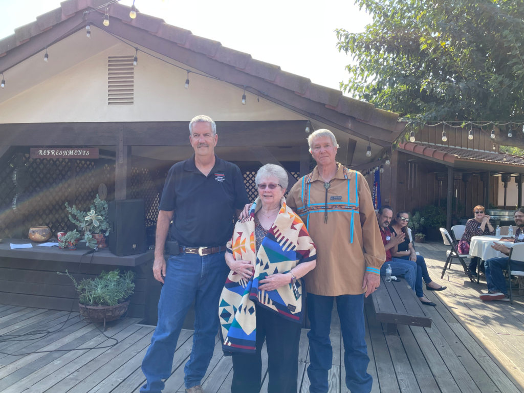 Two CPN legislators stand with a Tribal elder wrapped in a Pendleton blanket.