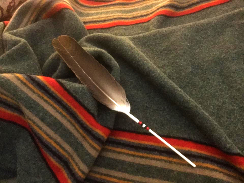 Brown feather with red, black and white beading on the shaft on a striped blanket.
