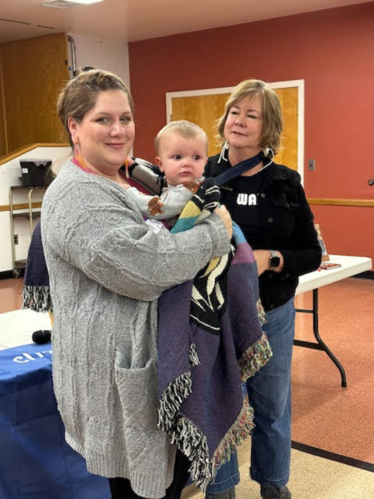 Eva Marie Carney stands next to a mother holding a baby wrapped in a blanket.
