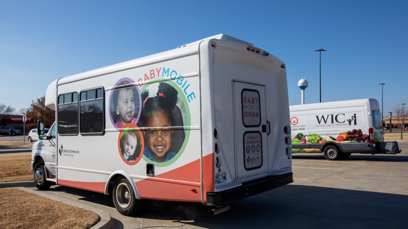 A large white van painted with the Infant Crisis Services' BabyMobile logo and colorful displays of smiling ghildren.