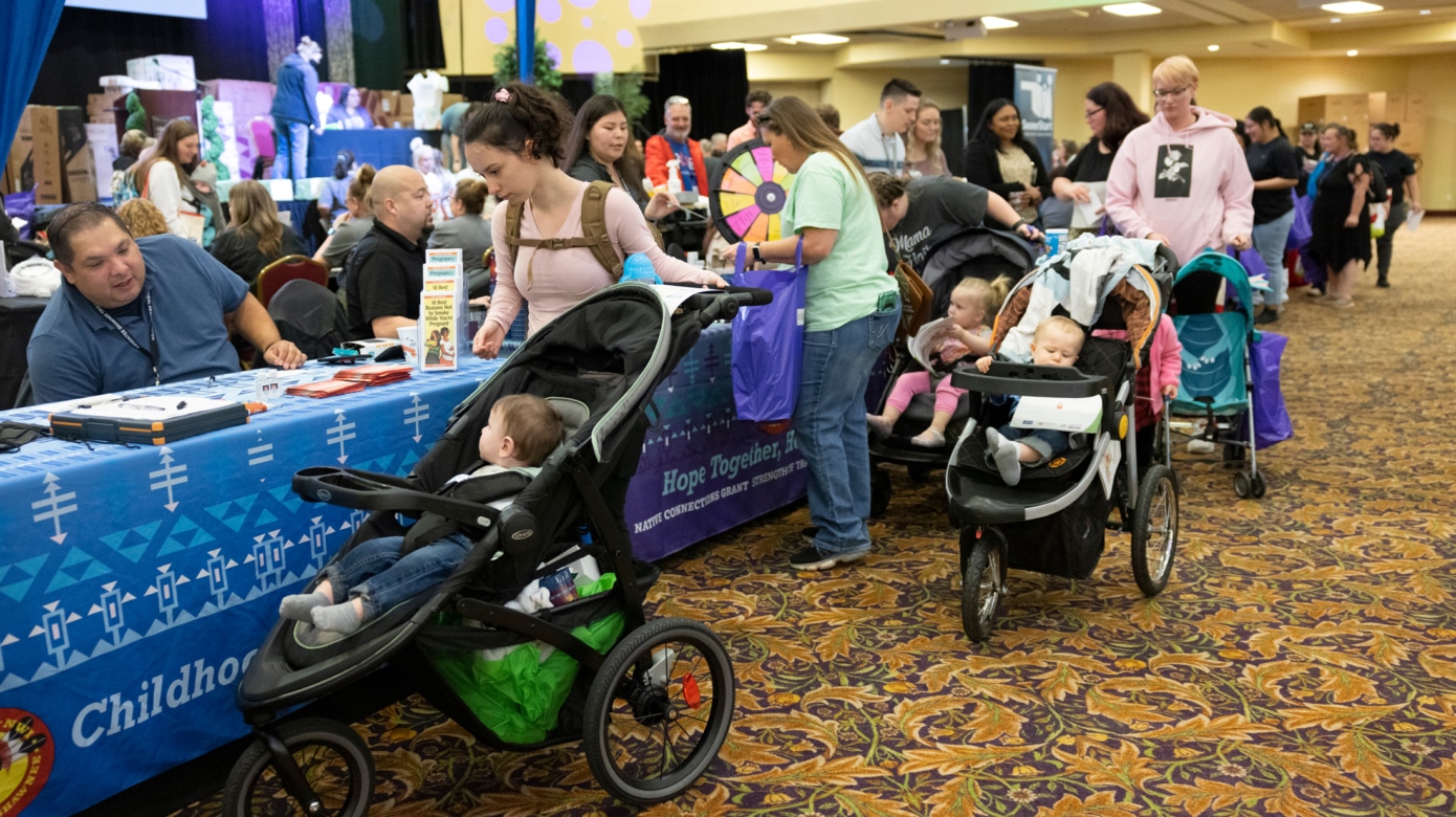 Several parents pushing strollers visit booths where local organizations share resources for parents and young children.