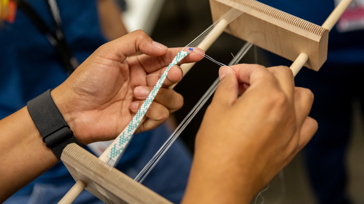 Close shot of hands beading on a loom. The artist is using white and light blue beads.