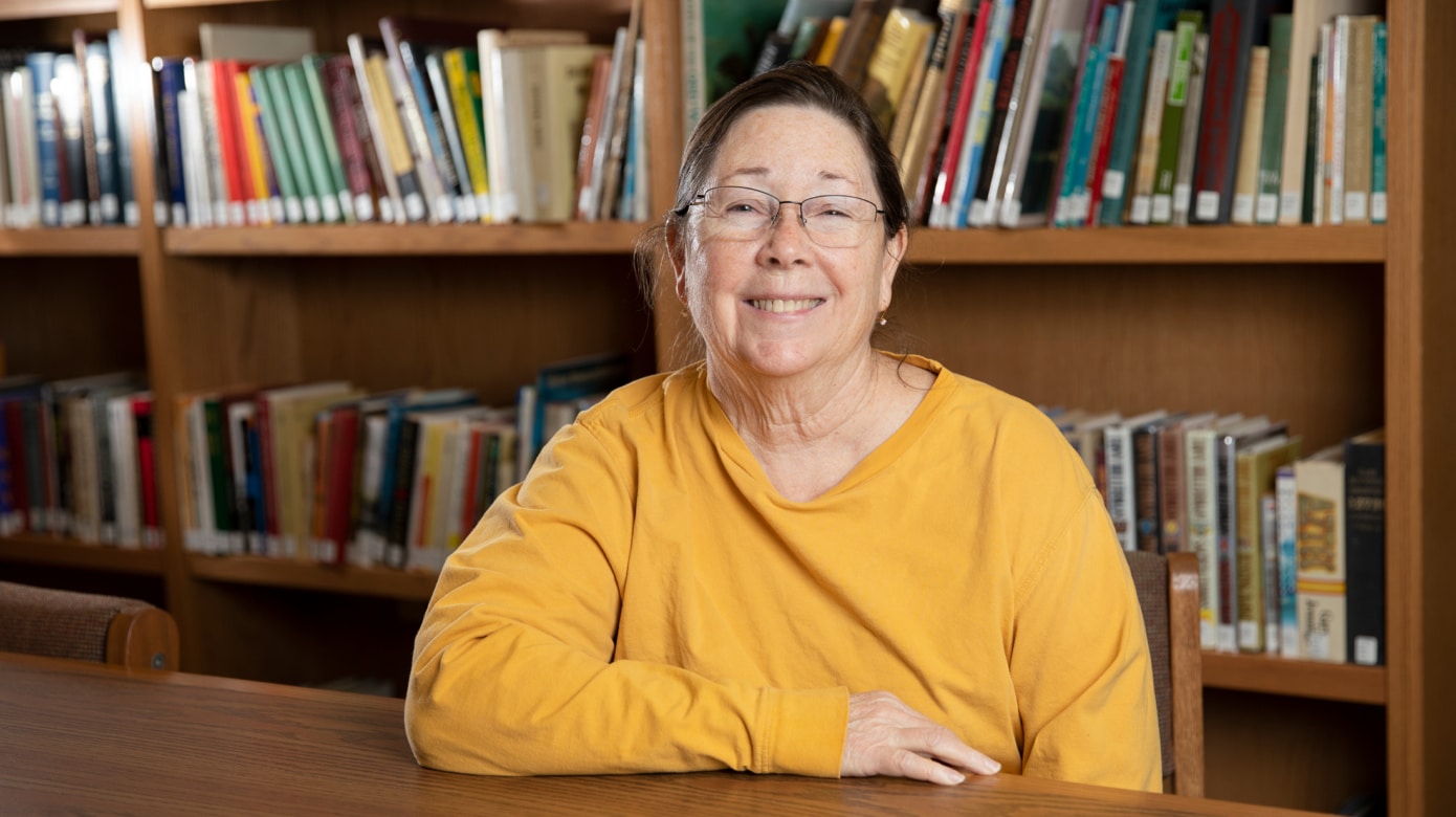Citizen Potawatomi Nation family history specialist Czarina Thompson sits in the CPN Cultural Heritage Center library surrounded by books. her golden yellow shirt and her smile bring a warmth to the photograph, reflecting what many feel when they talk with Thompson.