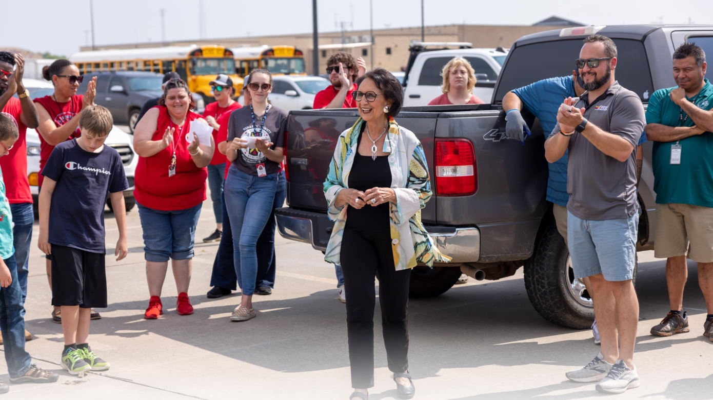 A group stands in a parking lot around CPN Vice-Chairman Linda Capps, clapping in response to her remarks.